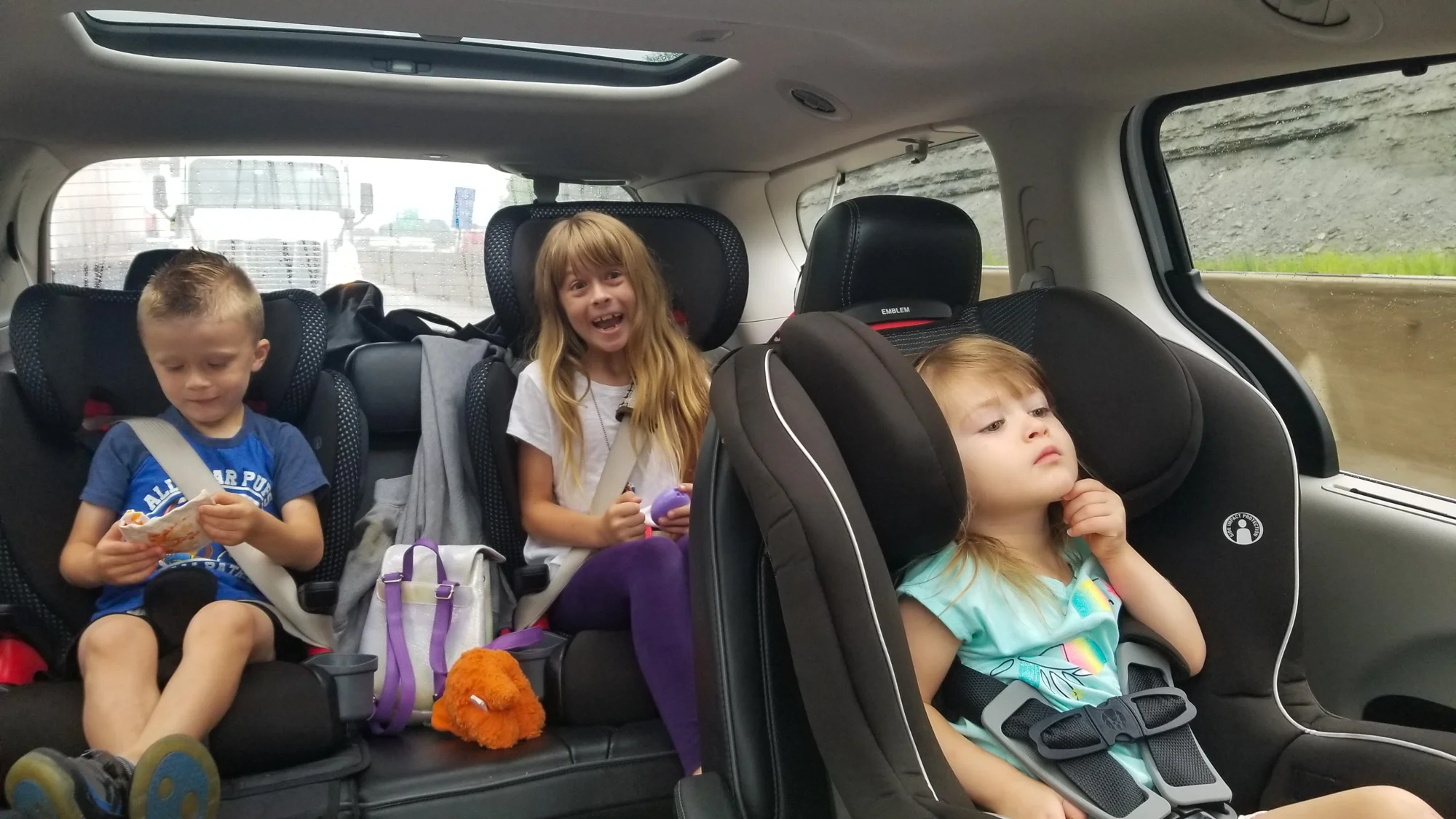 Traveling with kids in a car. Three children inside van carseats.