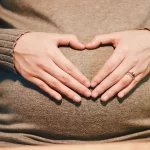 Woman holding hands in heart shape on belly for helpful pregnancy gifts for first time moms